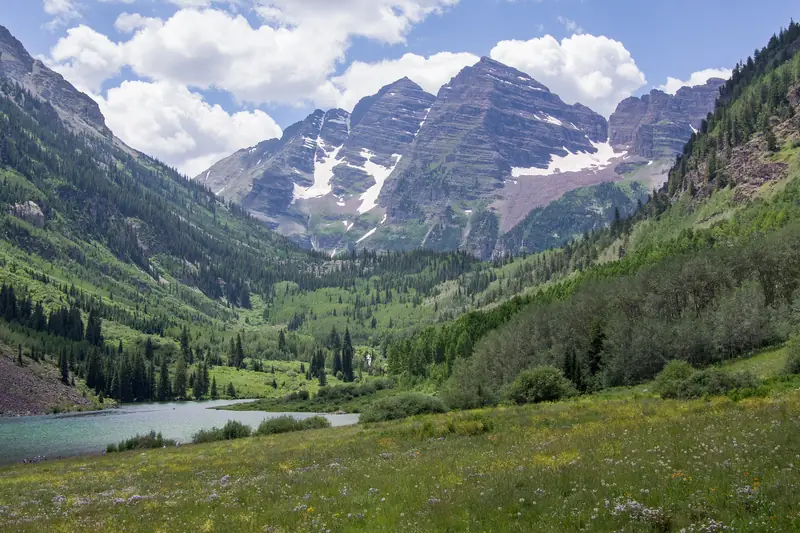 The Maroon Bells, streaked with old snow, rising above green slopes at the edge of Maroon Lake in summer