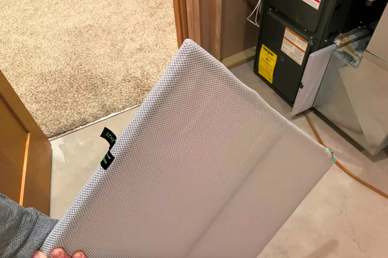 Hand holding a large white washable filter in front of a furnace whose lower access panel has been taken off